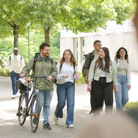 Studierende gehen gemeinsam über den hohenheimer Campus, einer schiebt ein Fahrrad.