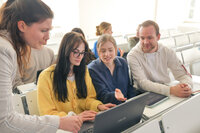 Studierende arbeiten gemeinsam an einem Laptop in einem Hörsaal.