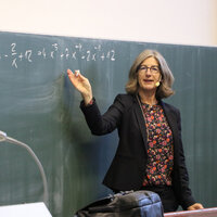Professorin erklärt mathematische Formel an der Tafel im Hörsaal.