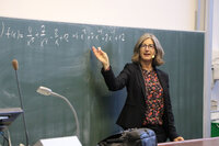 Professorin erklärt mathematische Formel an der Tafel im Hörsaal.