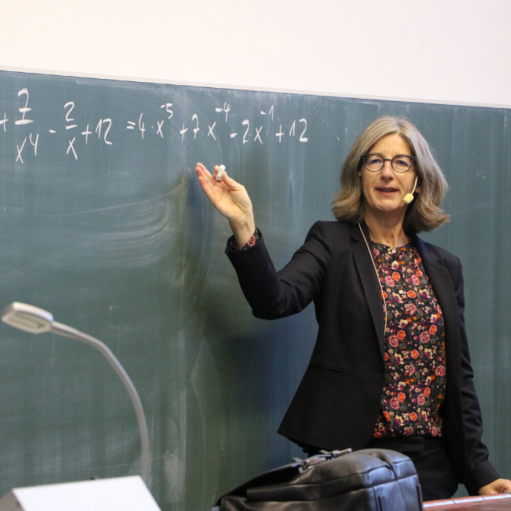 Professorin erklärt mathematische Formel an der Tafel im Hörsaal.