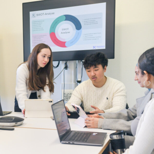 Gruppe von Studierenden diskutiert an einem Konferenztisch mit Laptops.