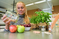 Studentin sitzt an einem Labortisch mit verschiedenen Lebensmitteln und Pflanzen vor sich